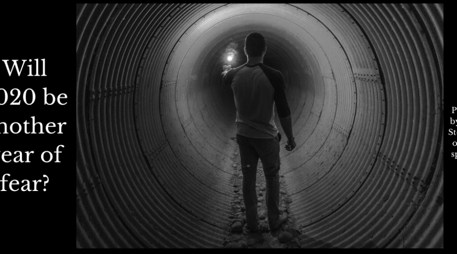 A man looking in fear down a human sized pipe with a flare to light his way.