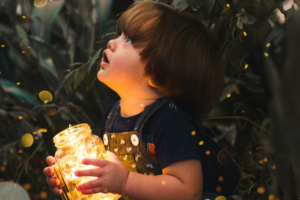 A little boy holding a yellow light in a glass jar.