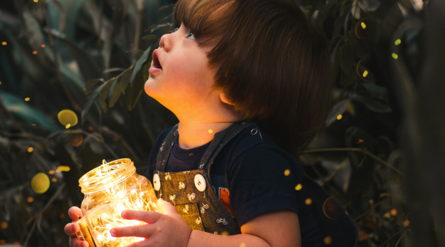 A little boy holding a yellow light in a glass jar.